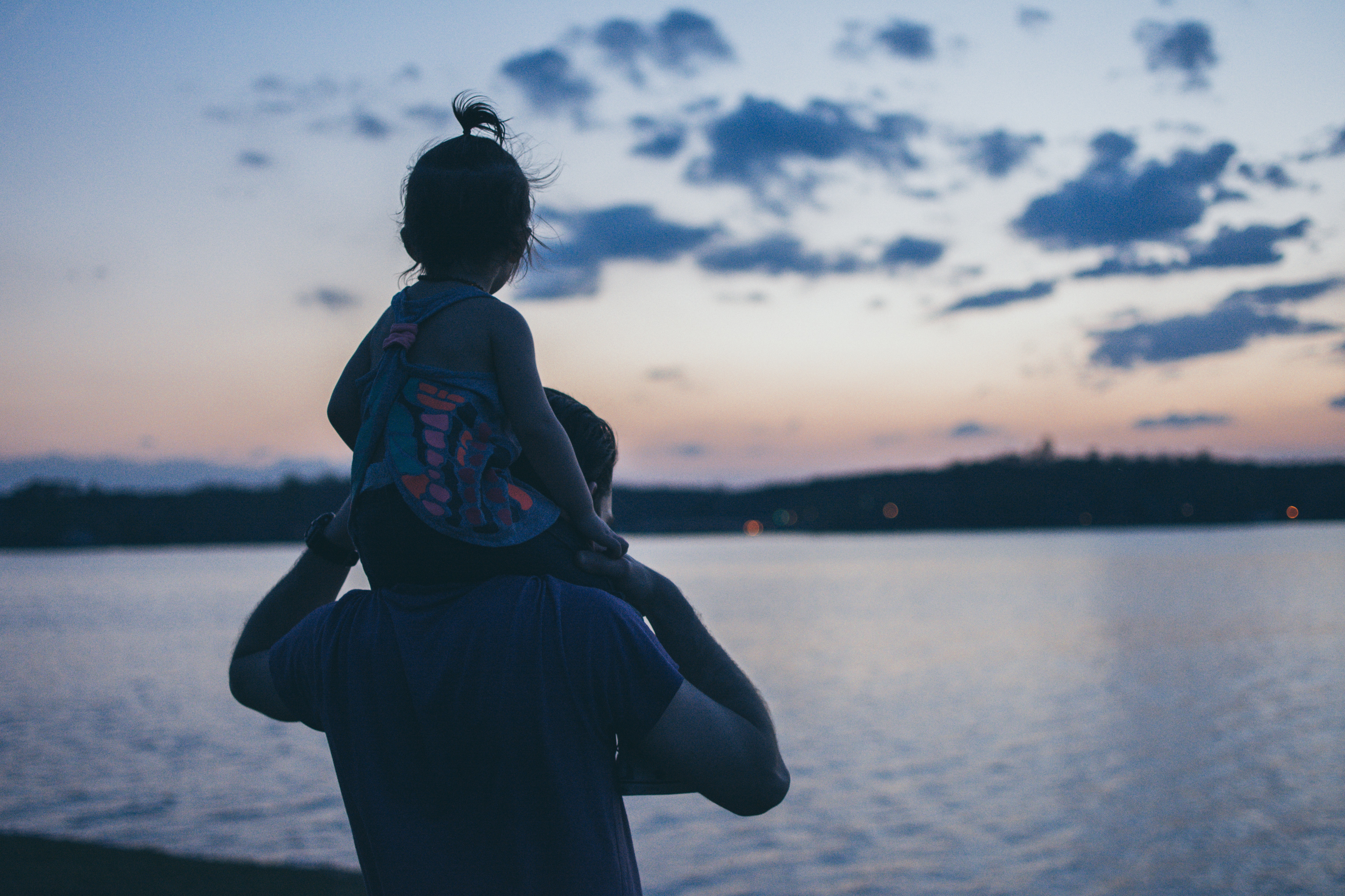 a girl on the piggyback of his father looking at the sea